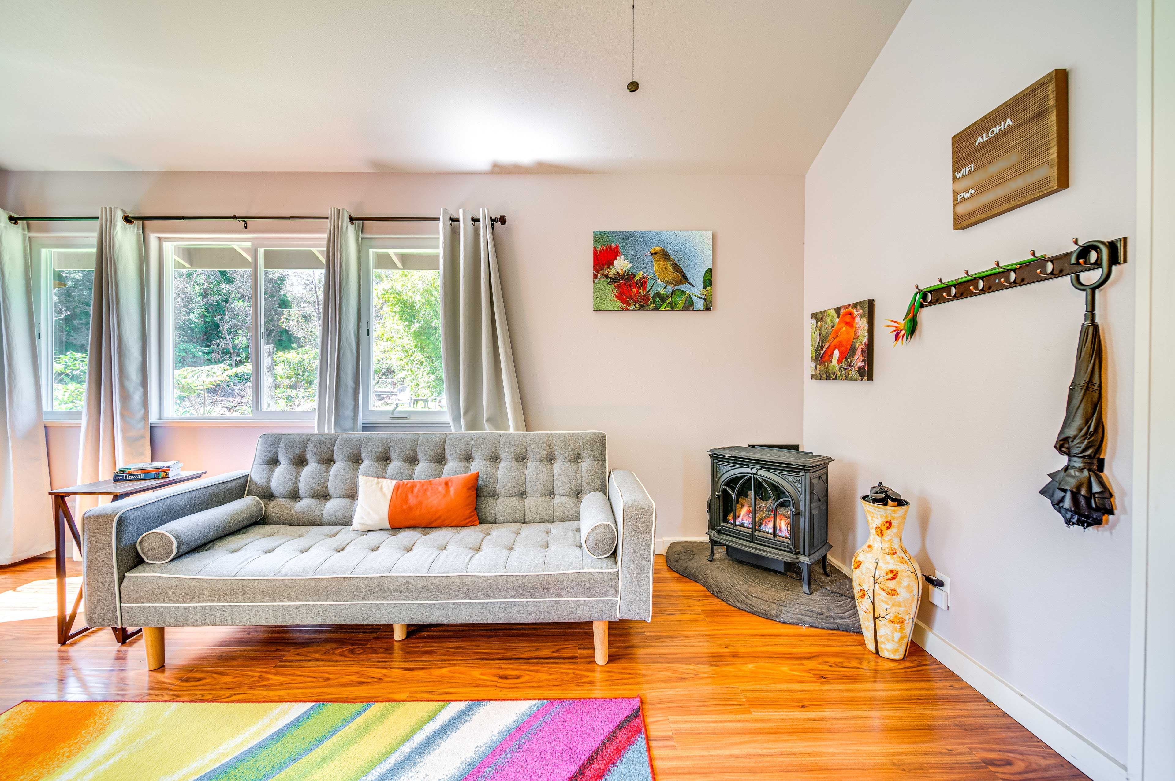 A living room with a grey sofa, a small table, a colorful rug, a fireplace, and artwork on the wall.