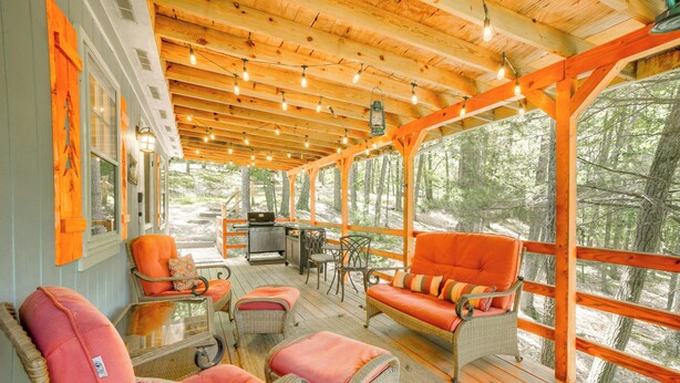 Une terrasse extérieure couverte, aménagée avec des meubles en osier, un barbecue et offrant une vue sur la forêt.
