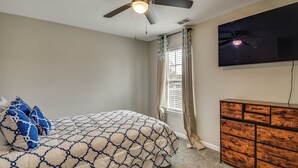 Un dormitorio con cama, ventilador de techo, cómoda y televisor en la pared.