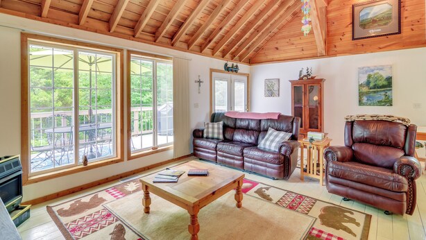 Ein geräumiges Wohnzimmer mit Holzboden, großen Fenstern, einem Ledersofa, einem Ledersessel und einem Kamin.