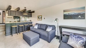 Un salon moderne avec un canapé gris, un pouf assorti et un coin bar équipé de tabourets.