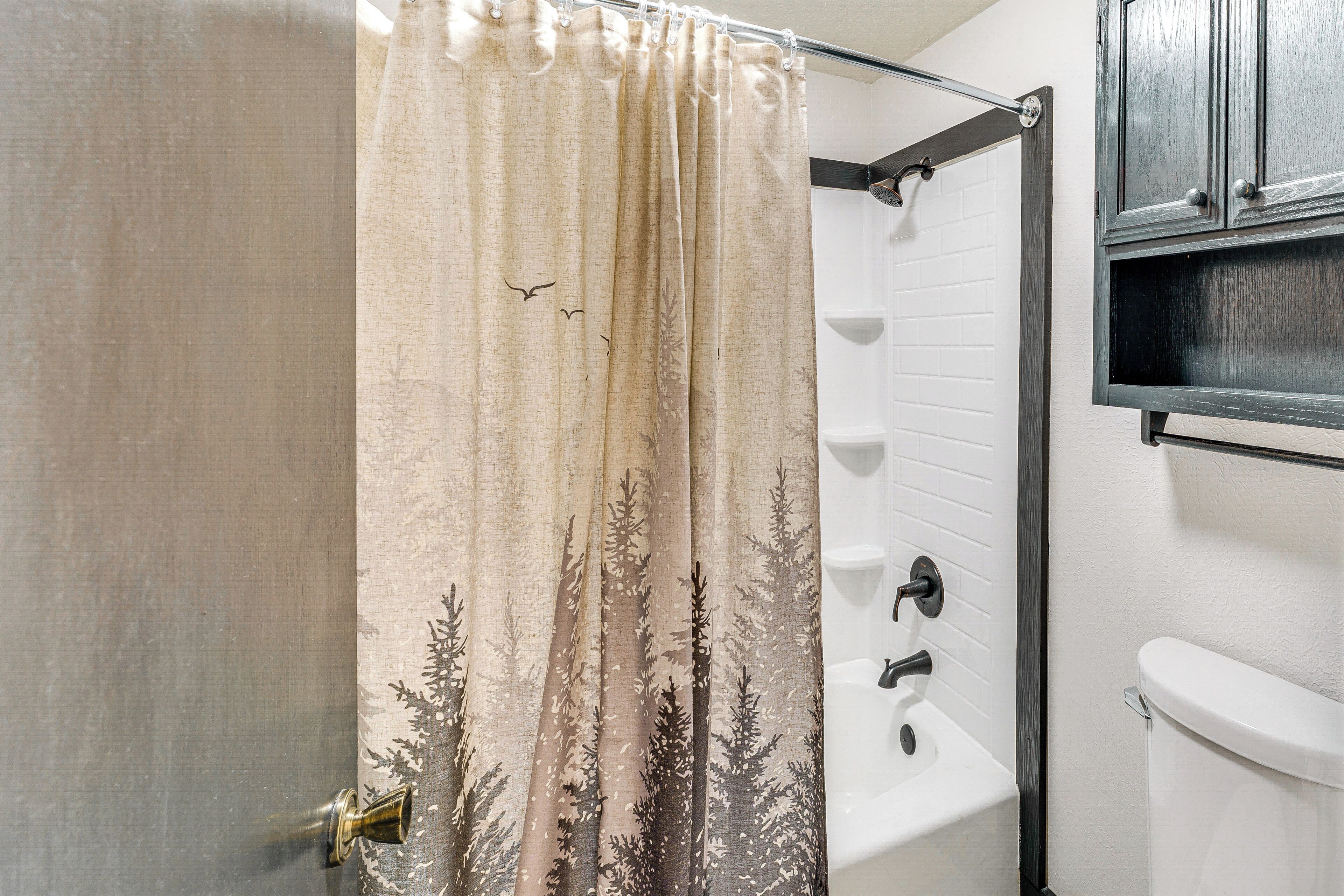 Ein Badezimmer mit Duschvorhang mit Waldmuster, einer weißen Badewanne und einer Toilette.