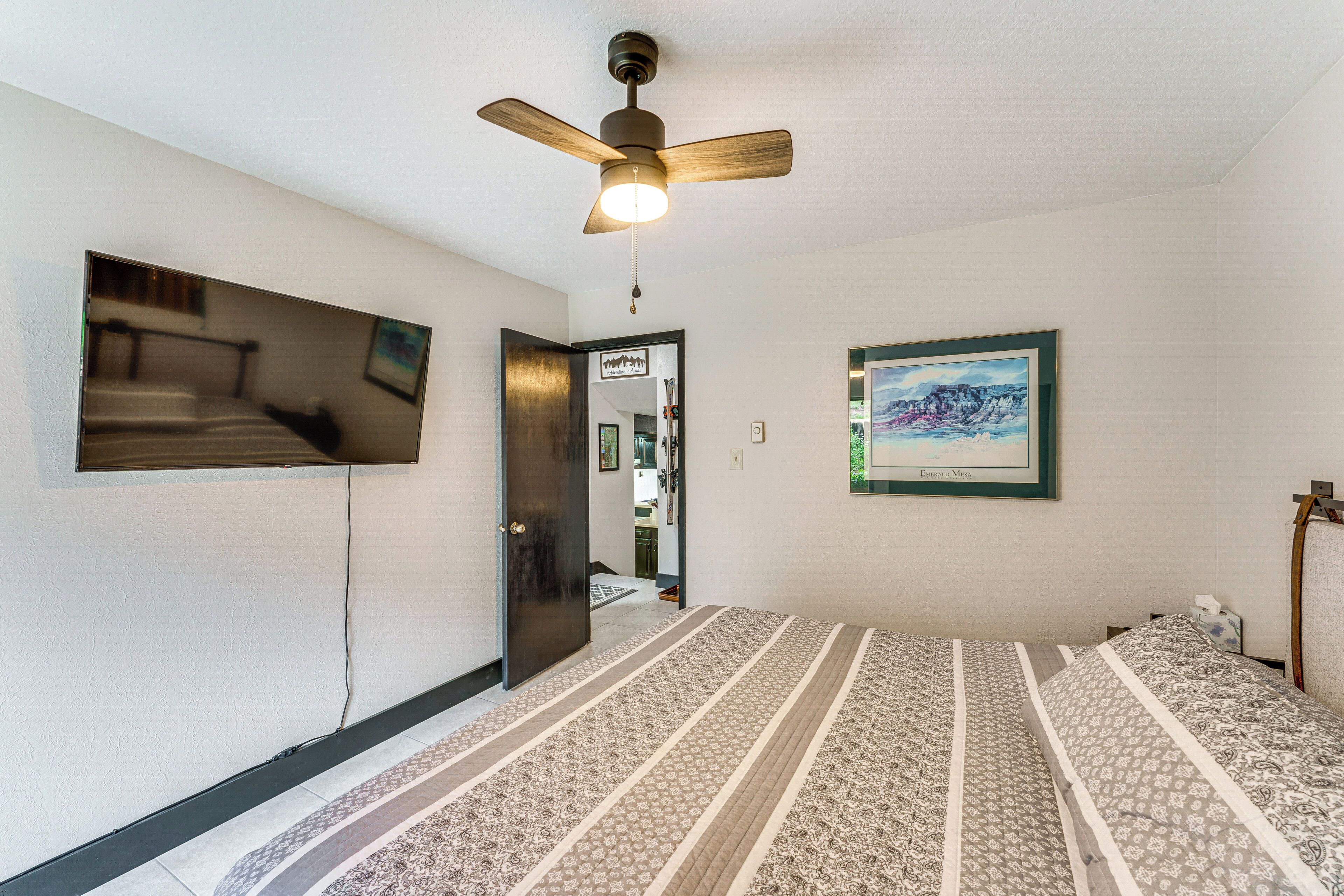 A bedroom with a bed, a ceiling fan, a TV mounted on the wall, and a framed picture.