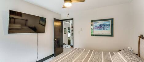 A bedroom with a bed, a ceiling fan, a TV mounted on the wall, and a framed picture.