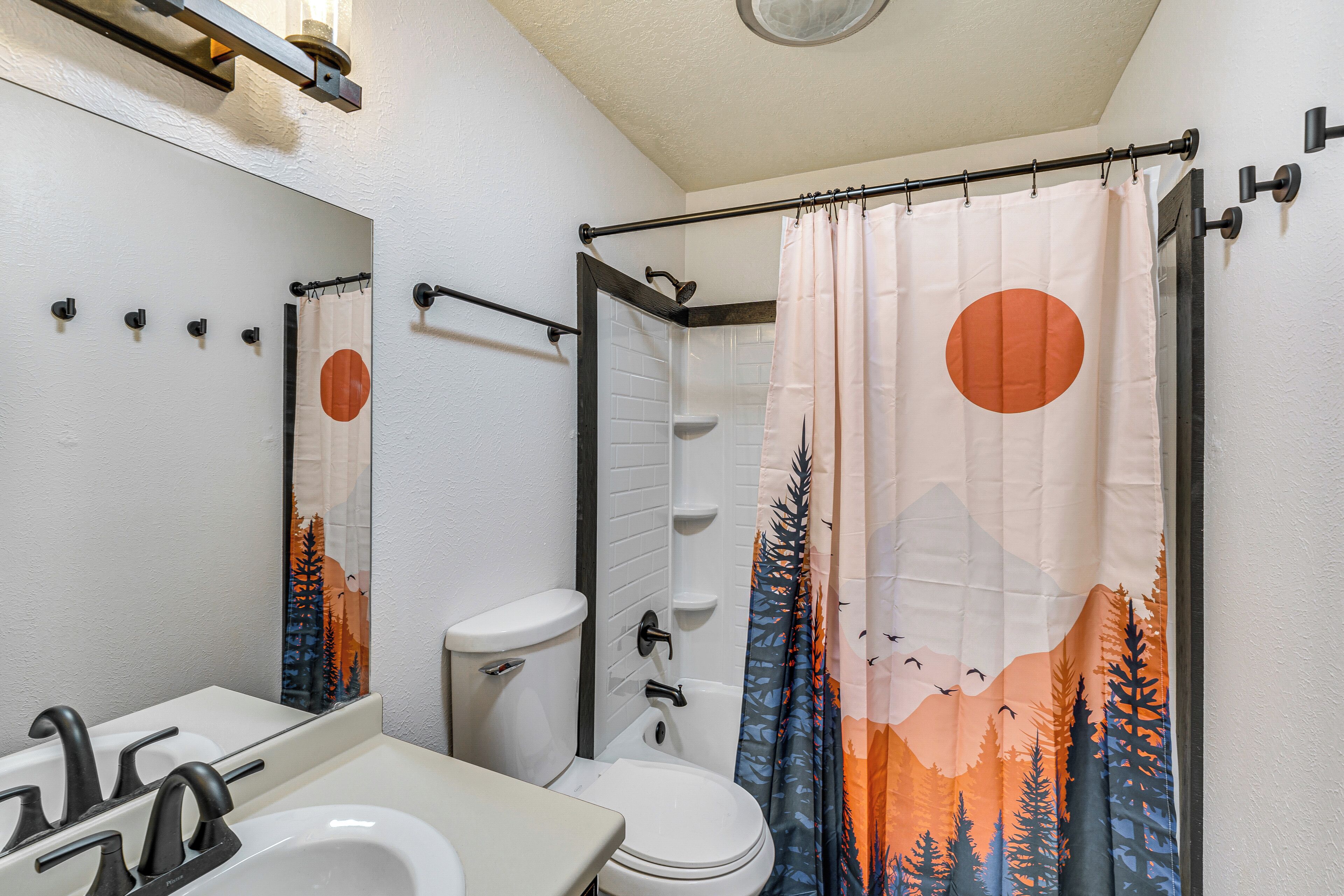 A bathroom with a white sink, a toilet, and a shower curtain with a forest and mountain design.