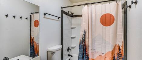 A bathroom with a white sink, a toilet, and a shower curtain with a forest and mountain design.