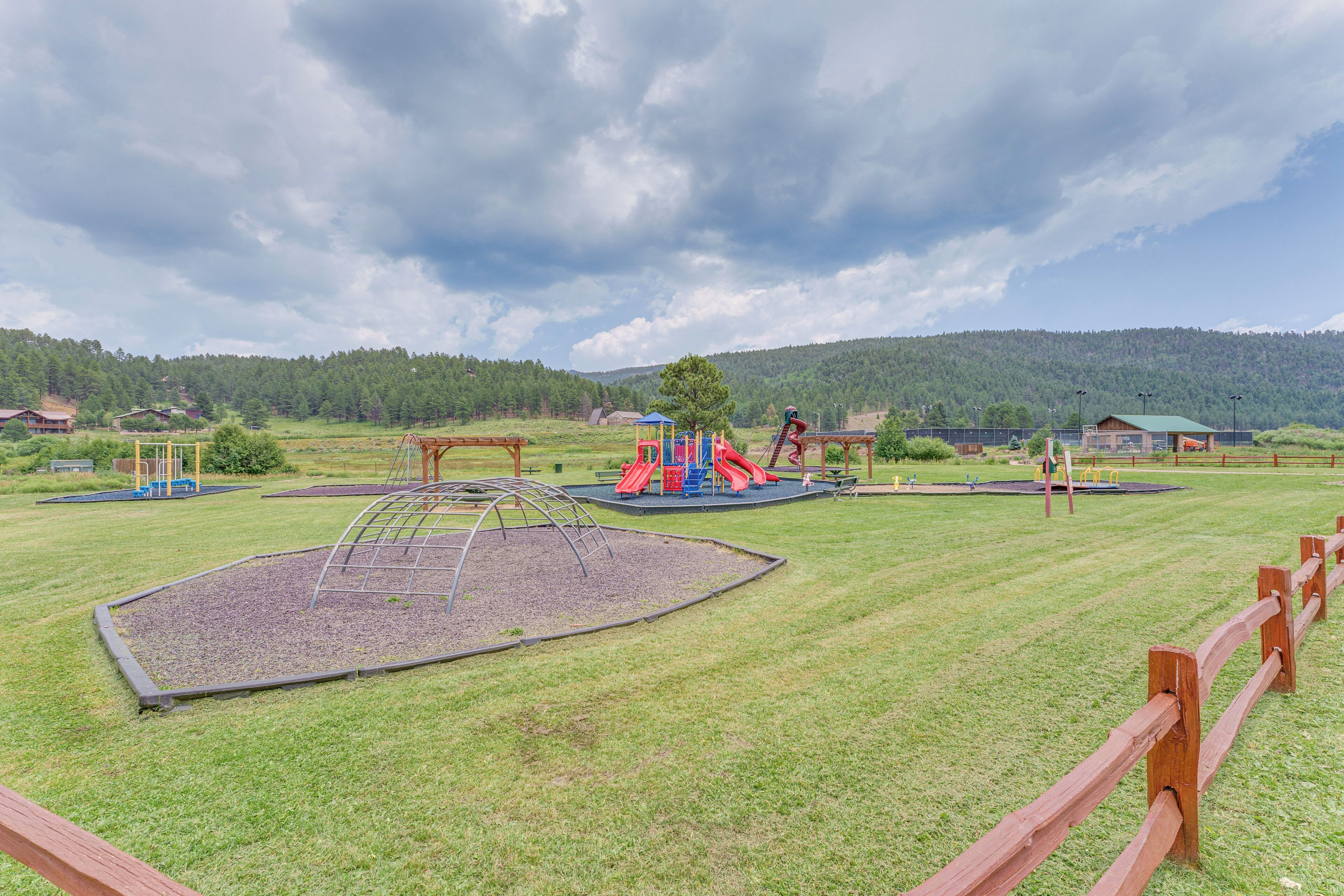 A playground with slides and climbing structures, surrounded by a wooden fence and grassy area.