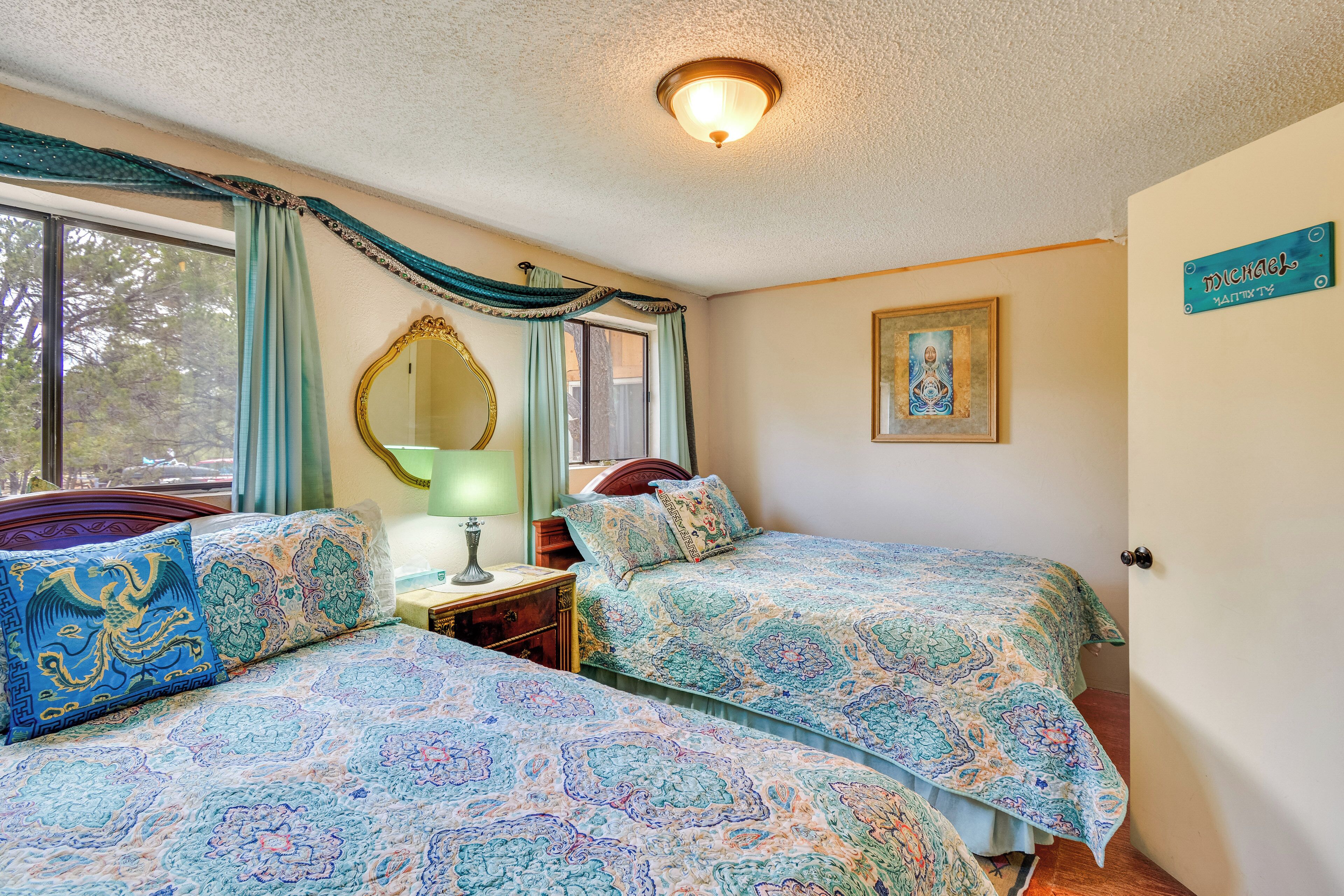 A bedroom with two beds, a mirror, a painting, and a sign on the wall.