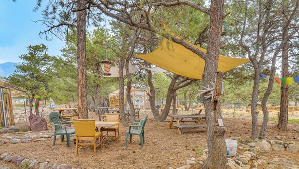 Zona salotto all'aperto con tavoli e sedie, circondata da alberi e rocce.