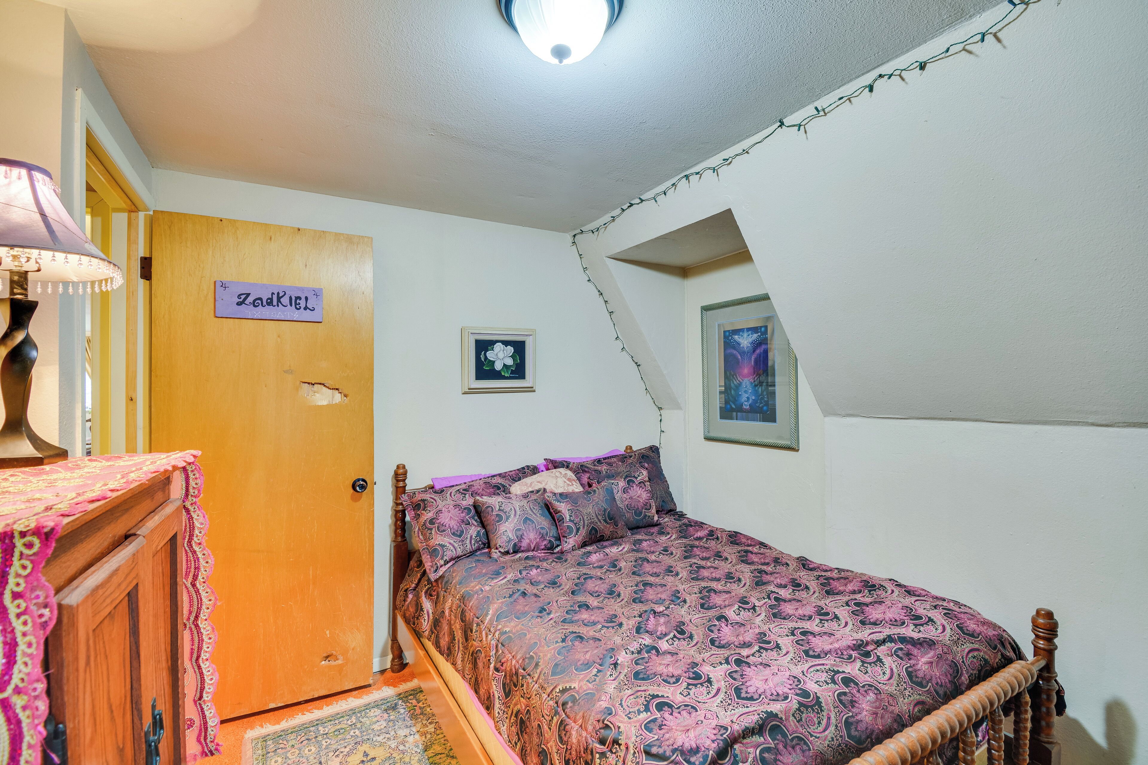 A bedroom with a bed, a wooden door, a lamp, and a rug.