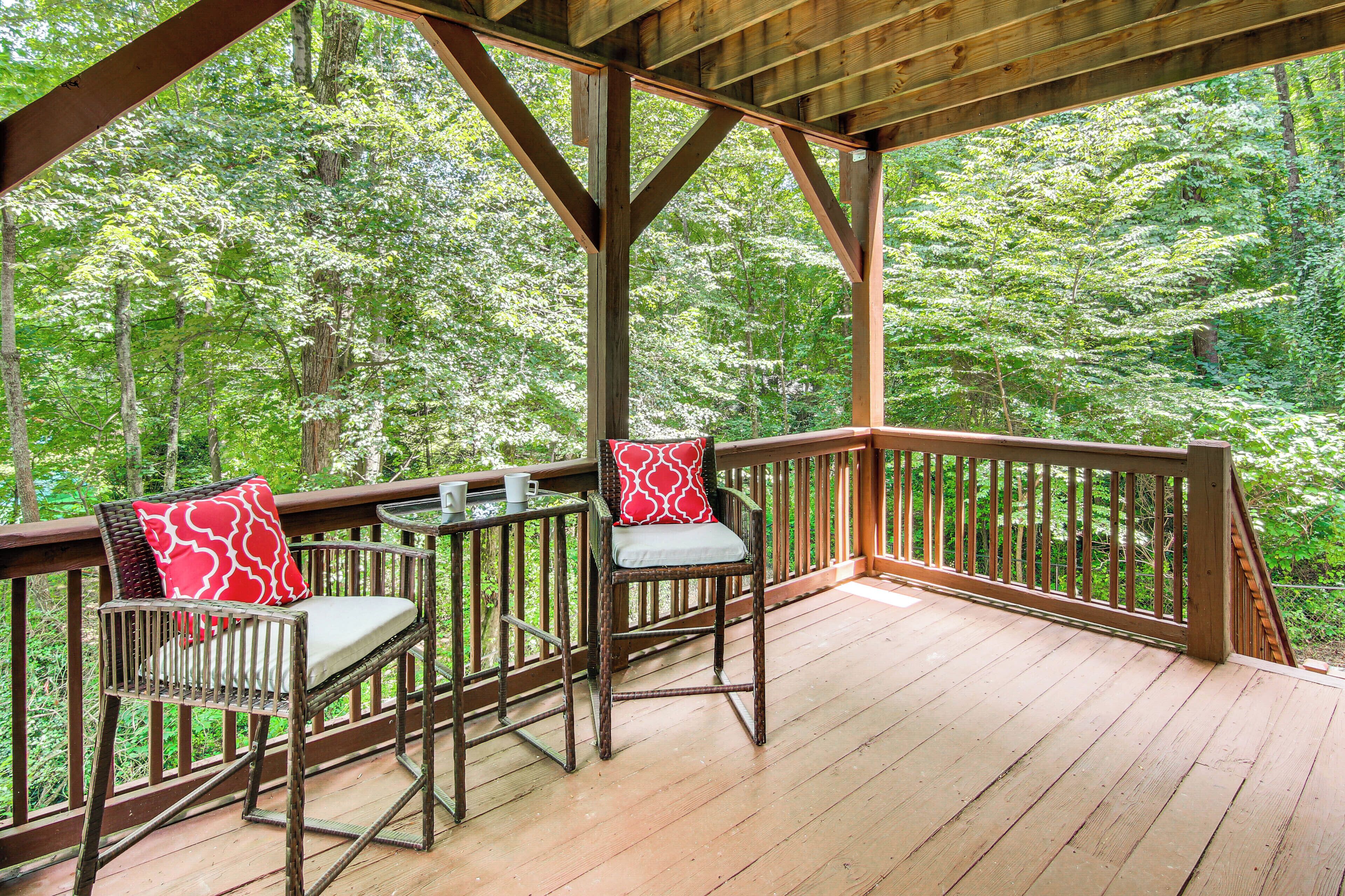 Une terrasse en bois avec deux chaises et une table, entourée d’une rambarde, donnant sur une zone boisée.