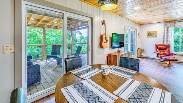 A spacious room with a wooden ceiling, a large window, a guitar, a TV, and a red chair. - Renovated Franklin Home w/ Mountain-view Deck! (Franklin)