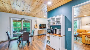 A modern kitchen with wooden cabinets, a dining area with a glass table, and a living room with a sofa and a TV. - Renovated Franklin Home w/ Mountain-view Deck! (Franklin)