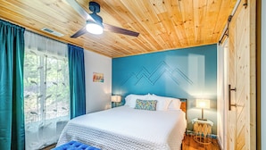 A bedroom with a bed, a blue bench, a ceiling fan, and a window with curtains. - Renovated Franklin Home w/ Mountain-view Deck! (Franklin)