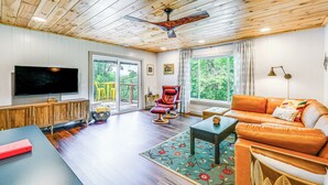 A spacious living room with a wooden ceiling, a large flat-screen TV, a leather sofa, a red chair, and a dining table. - Renovated Franklin Home w/ Mountain-view Deck! (Franklin)
