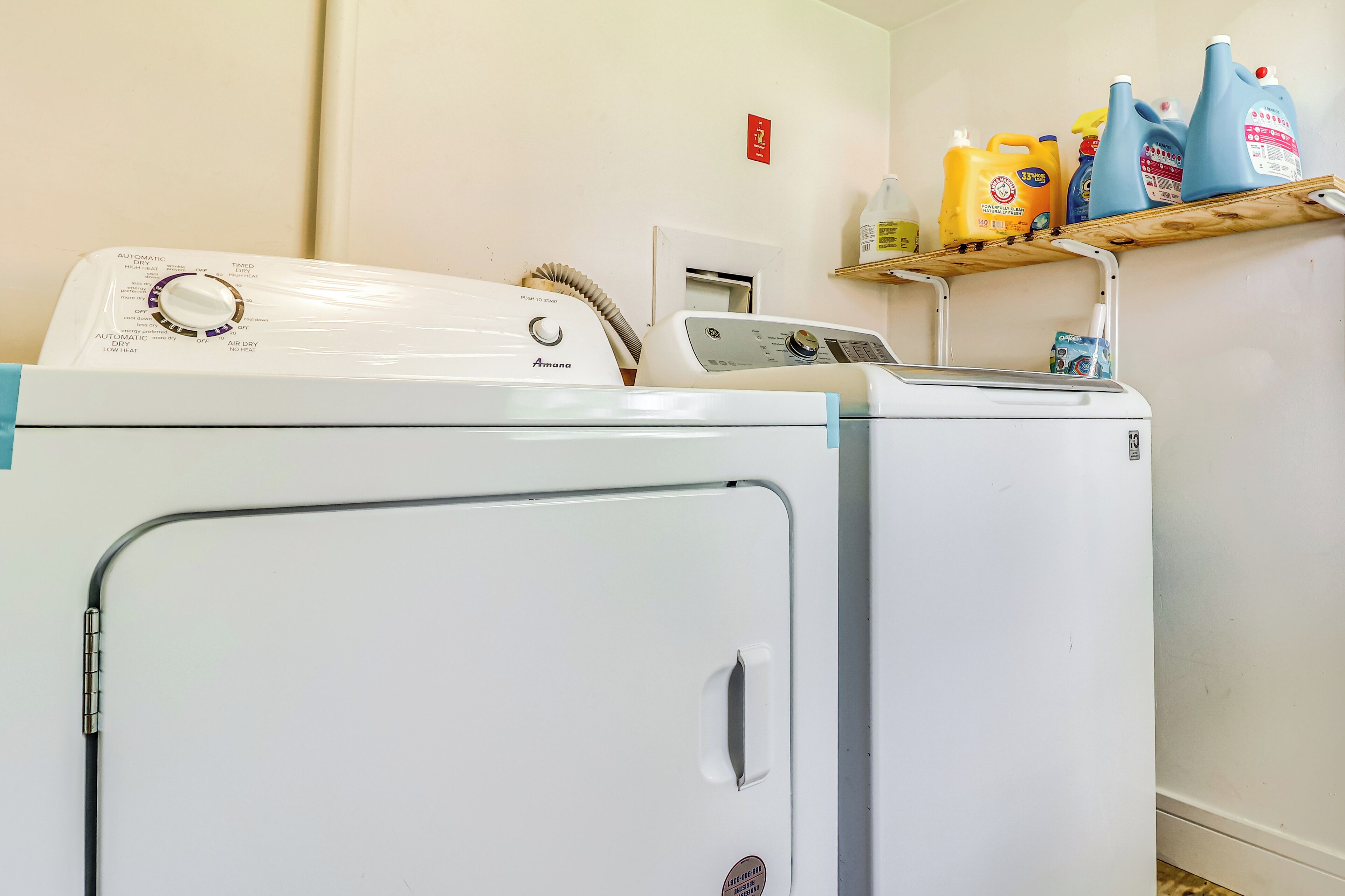 A laundry area with two washing machines and a shelf with detergent bottles.