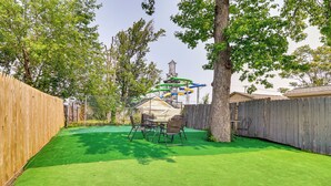 Un jardin avec une pelouse artificielle, une clôture en bois et une structure de toboggan en métal.