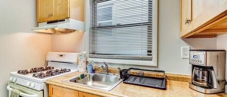 A kitchen with wooden cabinets, a stove, a sink, a toaster, and a window with blinds.