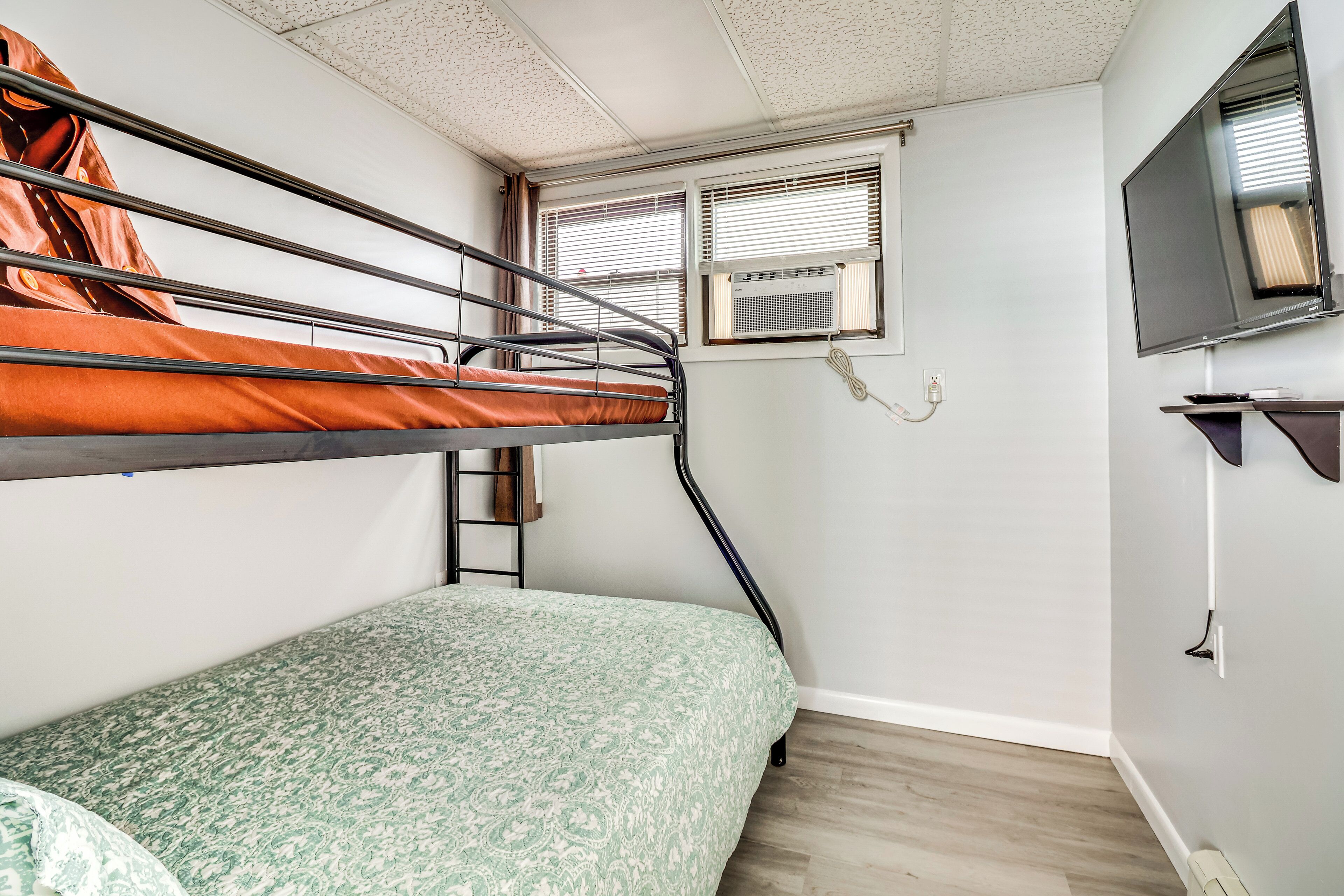 A bunk bed room with a patterned bedspread, a television on the wall, and an air conditioning unit.