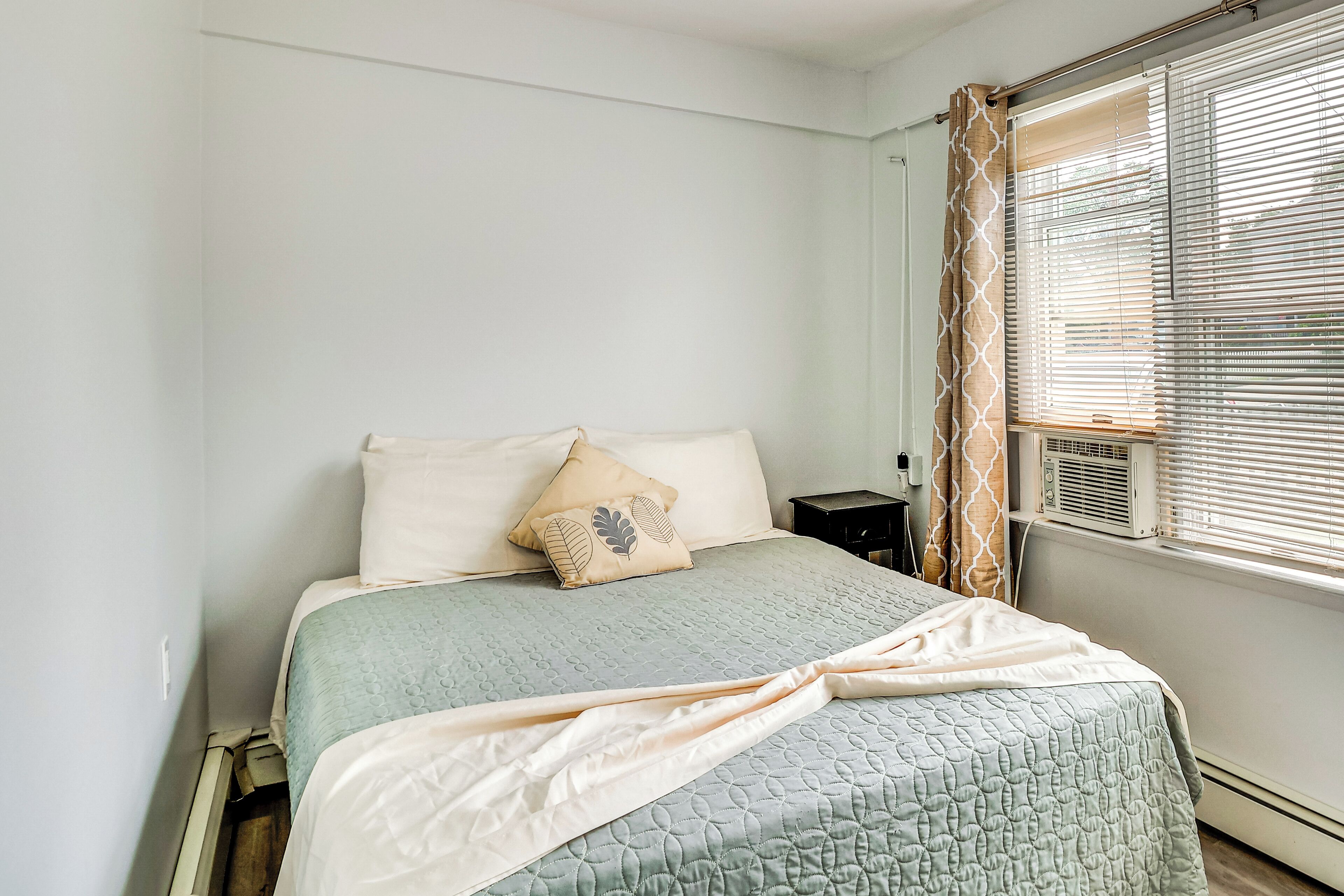 Een slaapkamer met een bed, kussens, een nachtkastje en een raam met zonwering.
