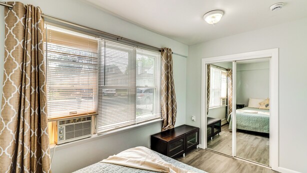Une chambre à coucher avec un lit, une commode, un miroir et une fenêtre avec des stores.