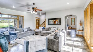 A spacious living area with a sectional sofa, a ceiling fan, and a large window offering a view of the outdoors. - Spacious Afton Home: Patio, Grill & Mountain Views (Afton)