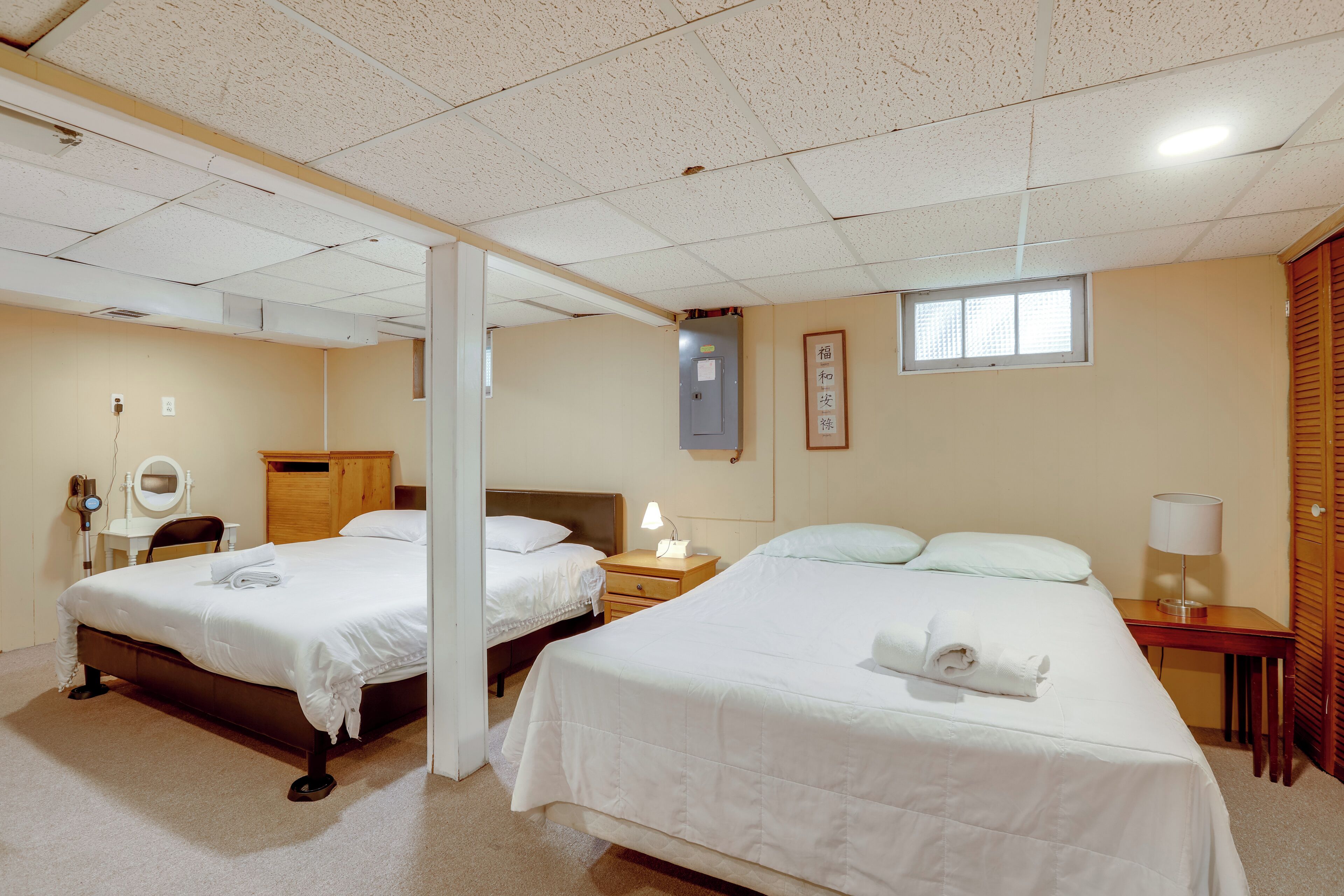Habitación de hotel con dos camas, un armario de madera, una mesita de noche con lámpara y un ventanal pequeño.