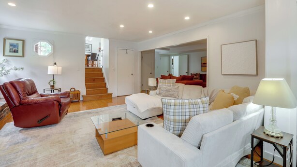 A spacious living room with a leather recliner, a white sofa, and a glass coffee table. A staircase leads to an upper floor, and a dining area is visible in the background. - Somerset Home w/ Large Yard Near Parks & Trails (Somerset)