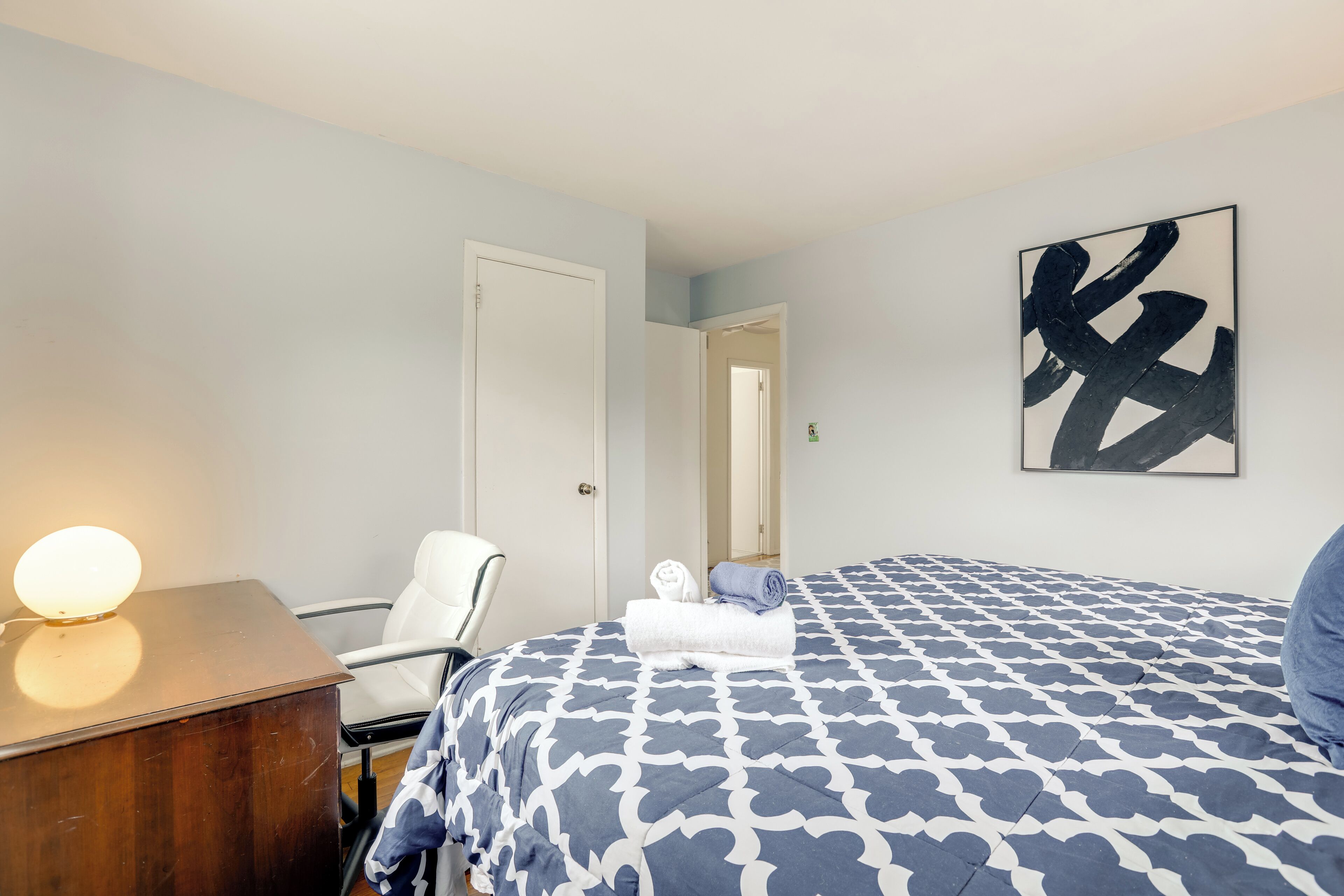 Una habitación de hotel con cama, escritorio con lámpara, una silla y una puerta.