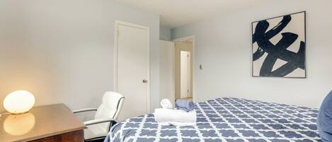 Una habitación de hotel con cama, escritorio con lámpara, una silla y una puerta.