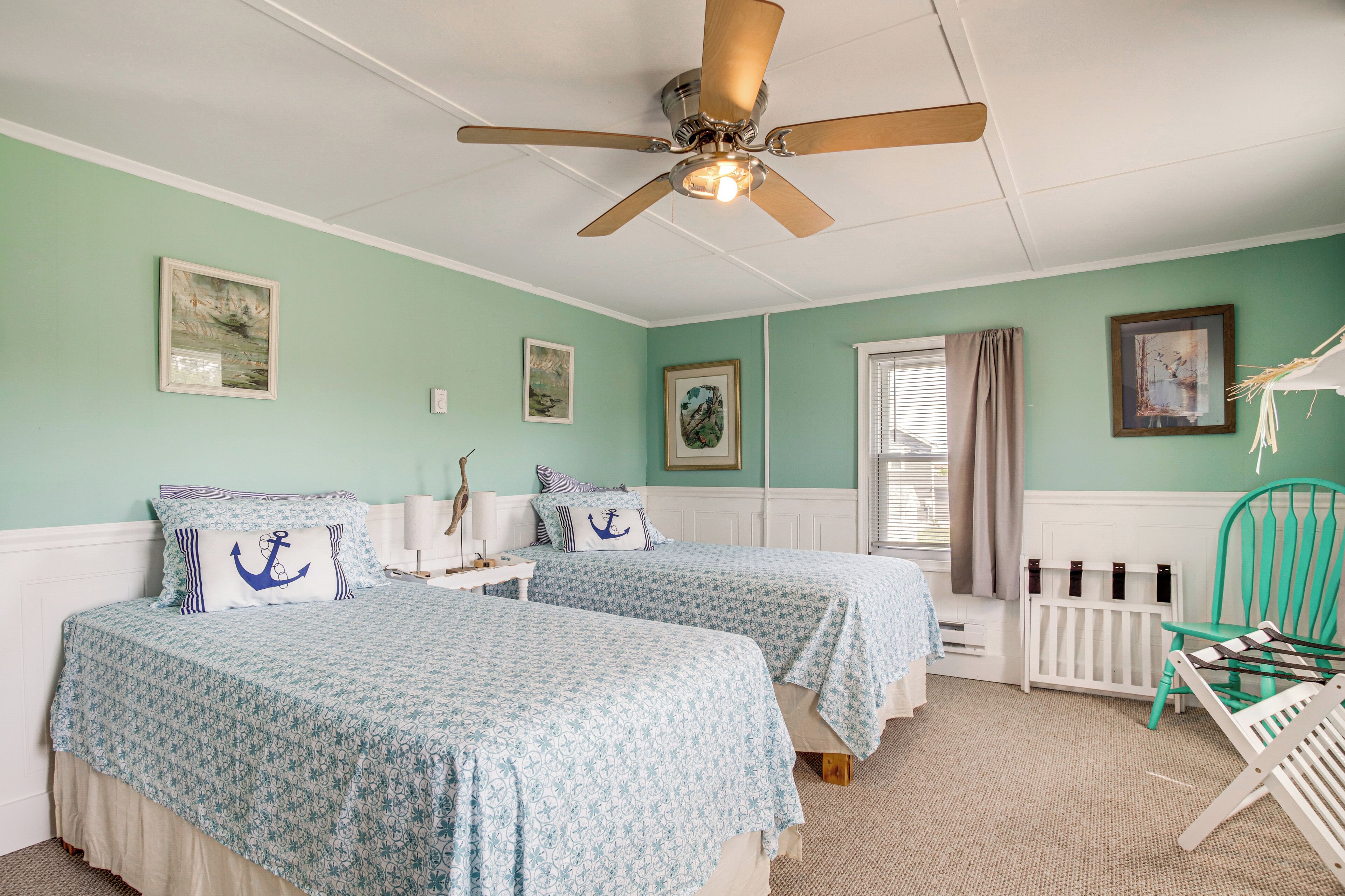 Une chambre avec deux lits, un ventilateur de plafond, une fenêtre avec des rideaux et un radiateur.
