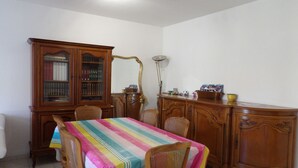 Ein Esszimmer mit einem Holzkabinett, einem Tisch mit bunter Tischdecke und Korbstühlen.