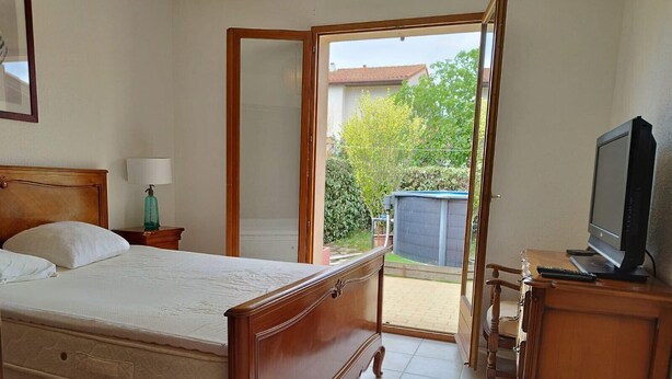 Ein Schlafzimmer mit einem hölzernen Bett, einem Fernseher auf einem Holzschrank und einer Glastür, die auf eine Terrasse führt.