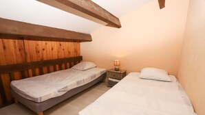 Une chambre avec deux lits simples, des poutres en bois, une table de chevet avec une lampe et une petite commode.