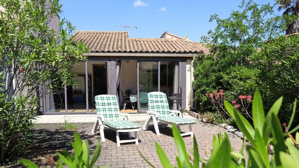 Un espace extérieur abrité avec deux fauteuils de jardin à motifs à carreaux, une table et une porte d’entrée en verre.