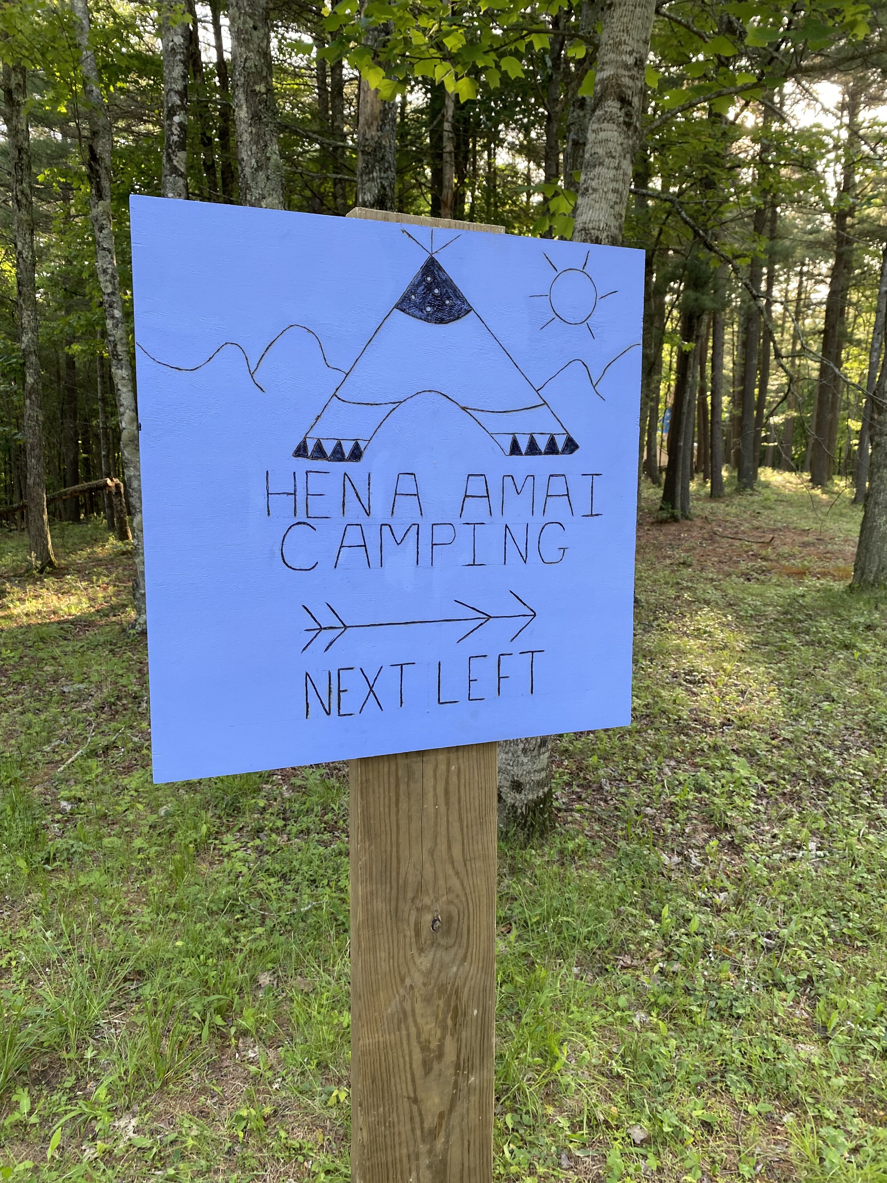 A sign for Hena Amaï Camping with a tent and arrow pointing to the left.
