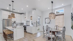 A modern kitchen with white cabinetry, a central island, and a dining area with a round table and chairs. - Bird Feather 160tai - C (Port Aransas)