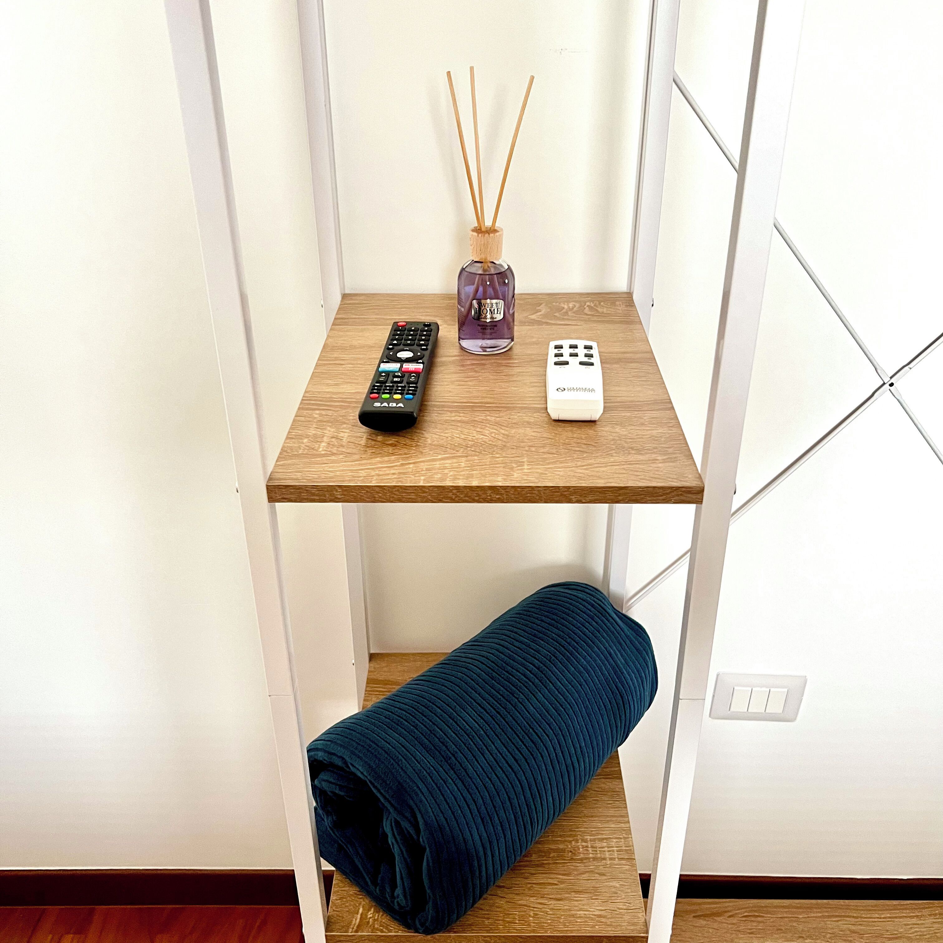 Ein kleines Holzregal mit einer Fernbedienung, einem Diffusor und einer zusammengerollten Matte.