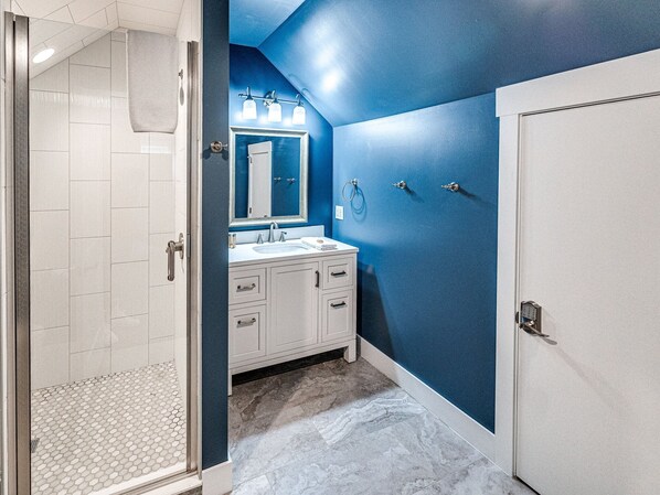 A bathroom with a walk-in shower, a double sink vanity, and a large mirror.