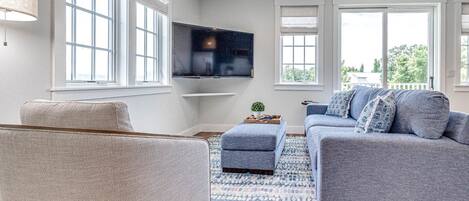 Una sala de estar moderna con un sofá gris, un sillón beige y un tapete azul estampado.