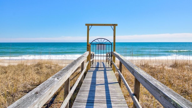 A wooden boardwalk leading to a beach with a metal gate structure.
