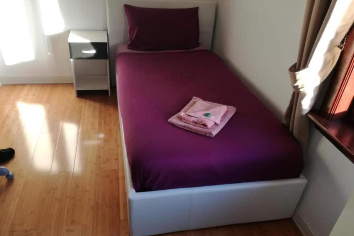 A small, neatly made bed with a purple bedspread and a folded towel on top.