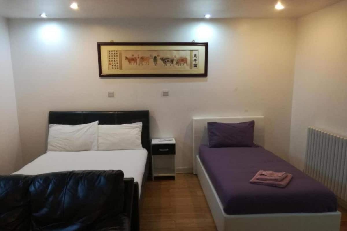 A bedroom with a bed, a bedside table, a nightstand, a chair, and a wall-mounted artwork.
