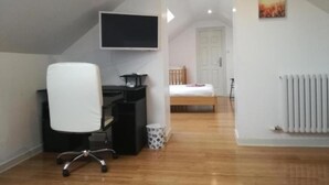 A small, well-lit attic bedroom with a wooden floor, a desk with a chair, a bed, a radiator, and a TV mounted on the wall. - Ardenlea House Hotel B&B (Aberdeen)
