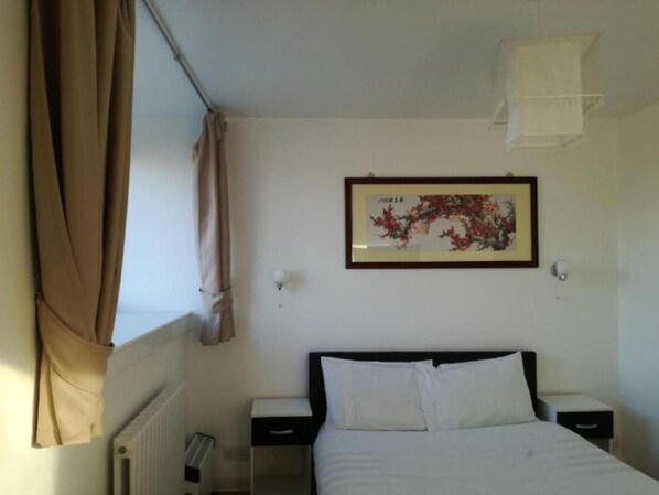 A hotel room with a bed, two bedside tables, a radiator, a window with curtains, and a framed picture on the wall. - Ardenlea House Hotel B&B (Aberdeen)