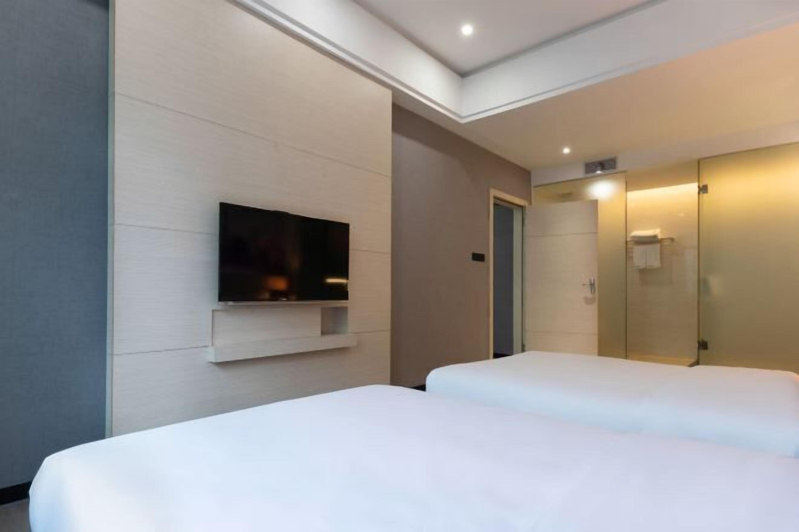 A hotel room with two beds, a flat-screen TV mounted on the wall, and a mirror on the wall.