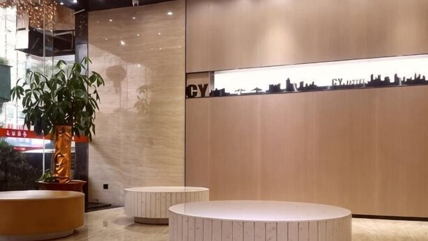 A reception area with a modern design, featuring a reception desk, a potted plant, and a seating area with a circular bench. - Caiyang Hotel (Haifeng)