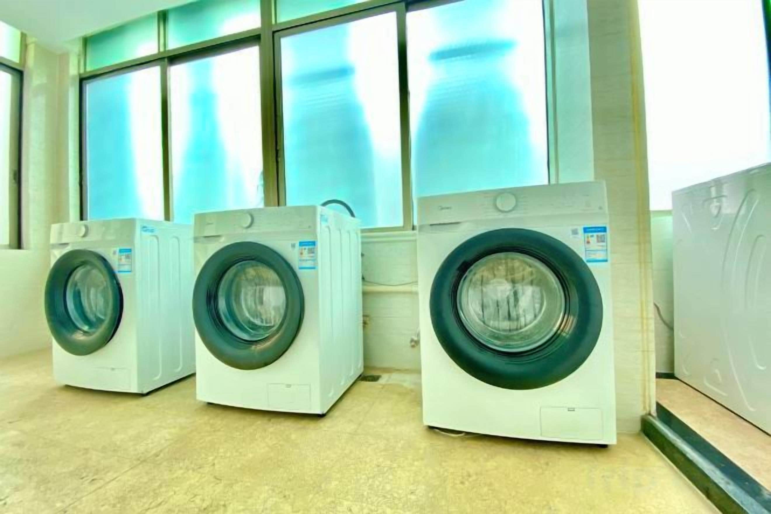 Three front-loading washing machines in a row, with large windows in the background.
