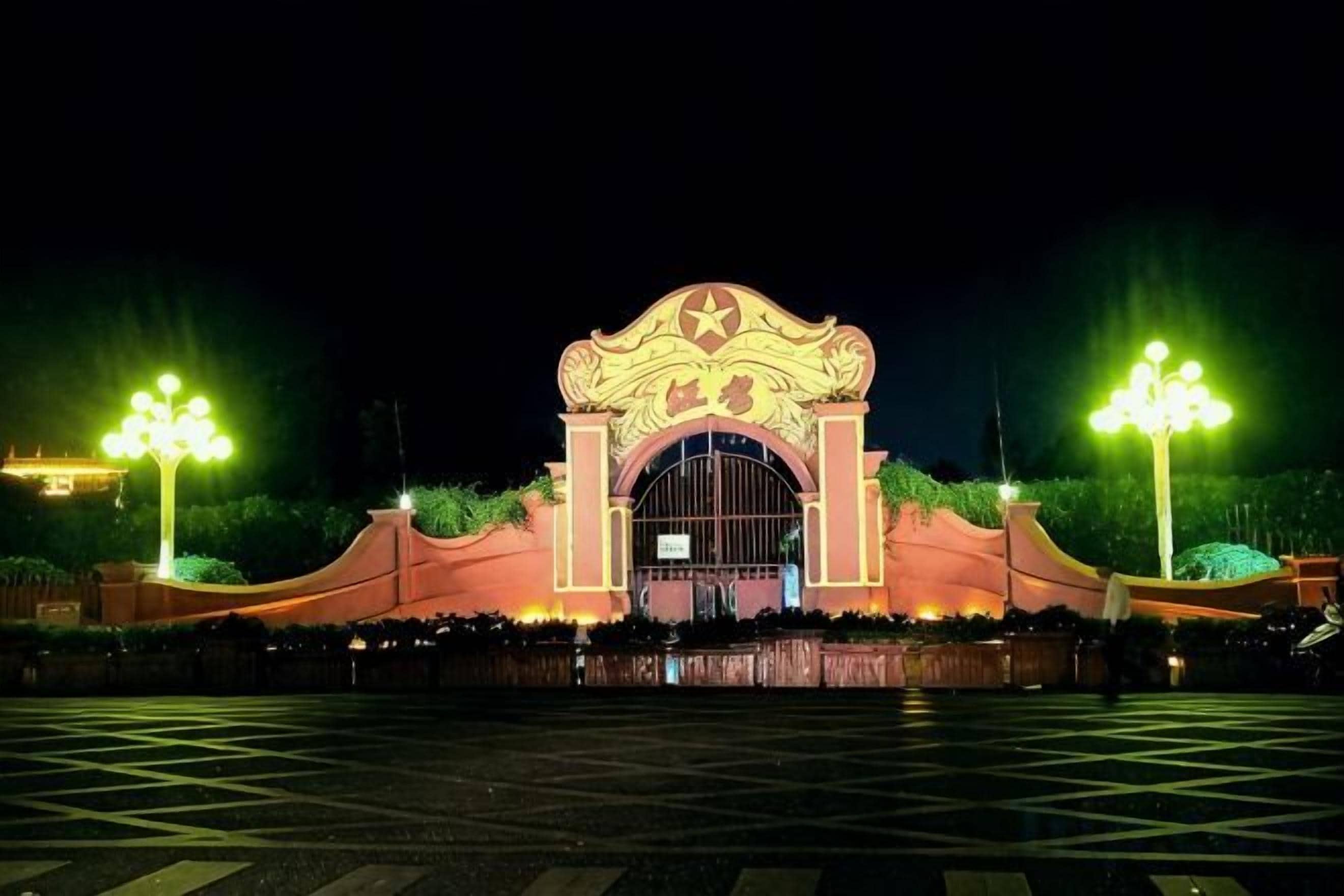 Une grande entrée illuminée, agrémentée d’une arche décorative, d’une zone pavée devant et de deux lampadaires.