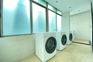 Una sala de bugaderia amb tres rentadores blanques i un gran finestral.